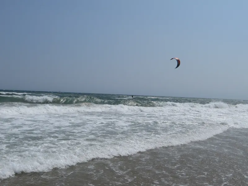 Kiteboarder riding the wind and waves along Cape Hatteras National Seashore, with colorful kite against the sky