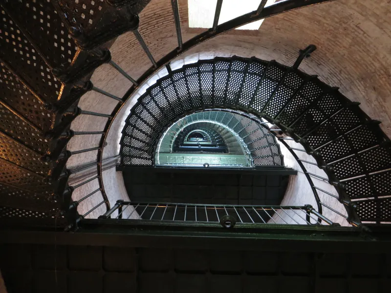 Currituck Beach Lighthouse in Corolla with the Victorian keeper's house visible at its base, surrounded by mature trees on the lighthouse grounds