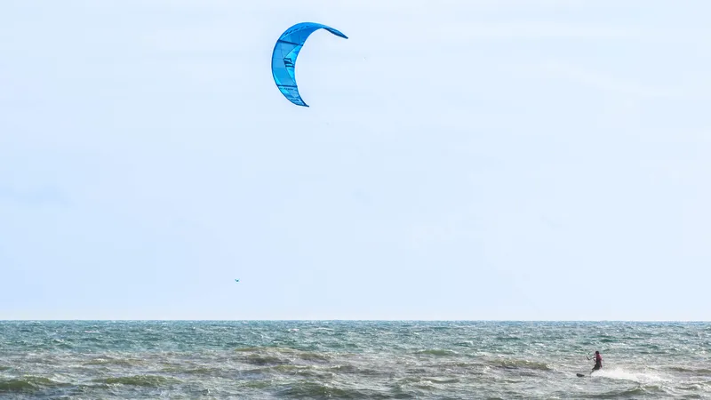 Kiteboarder launching over waves off Hatteras Island with kite visible against a bright sky