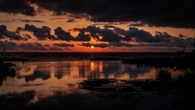Vivid sunset sky over Currituck Sound from the Duck boardwalk, with silhouetted railing posts and warm reflections on the water