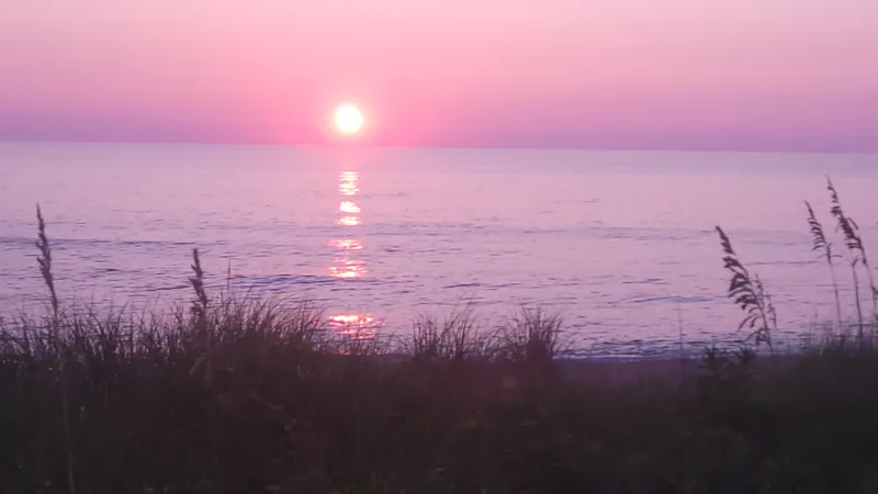 Sunrise over the Atlantic Ocean at Duck, NC with warm orange and pink light reflecting on wet sand at the waterline
