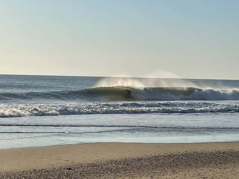 A surfer resting in the shade of a beach umbrella on the wide sandy beach north of Buxton Village on Hatteras Island