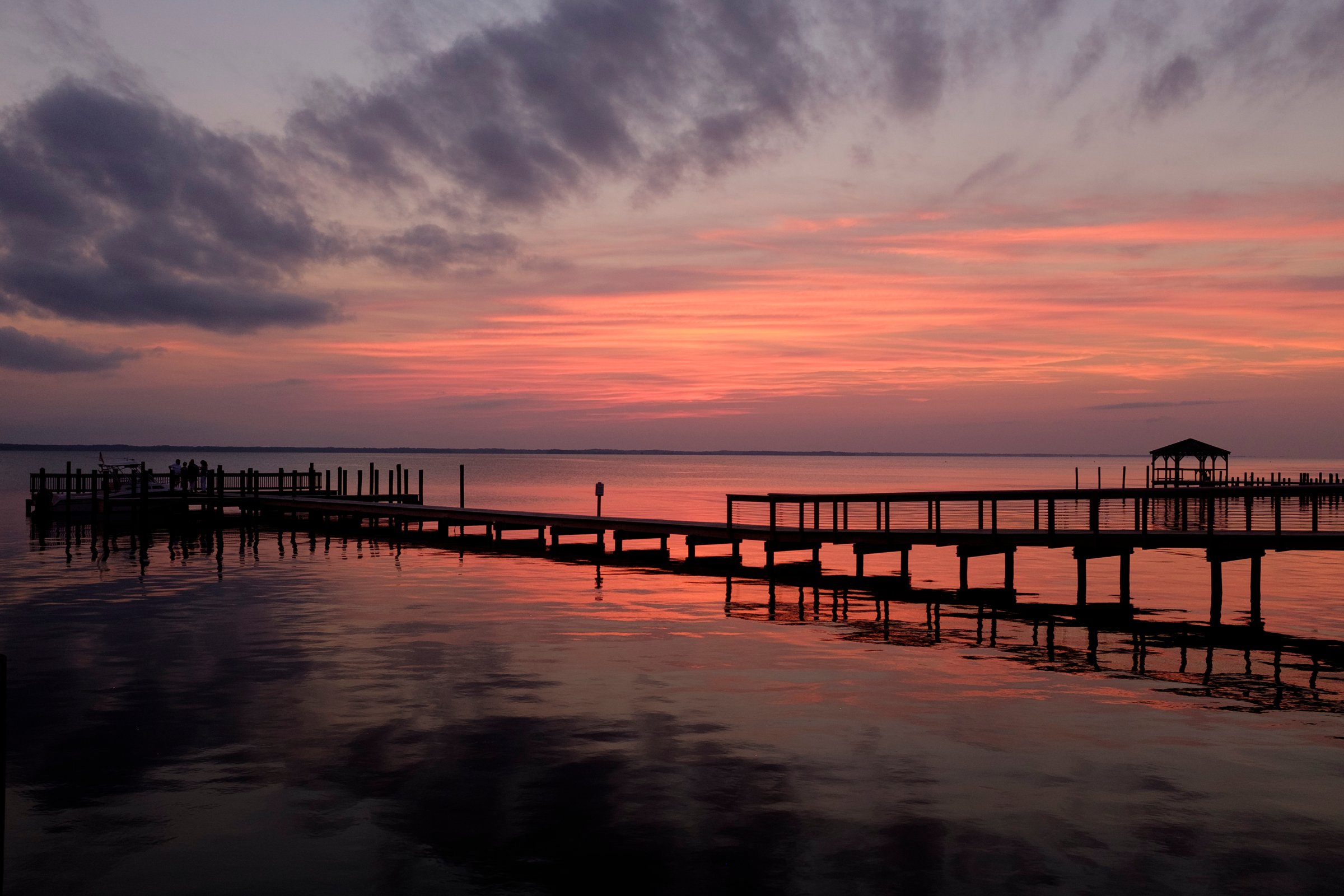 Golden sunset over Currituck Sound viewed from the Duck boardwalk, with wooden railings in the foreground and calm water reflecting the sky