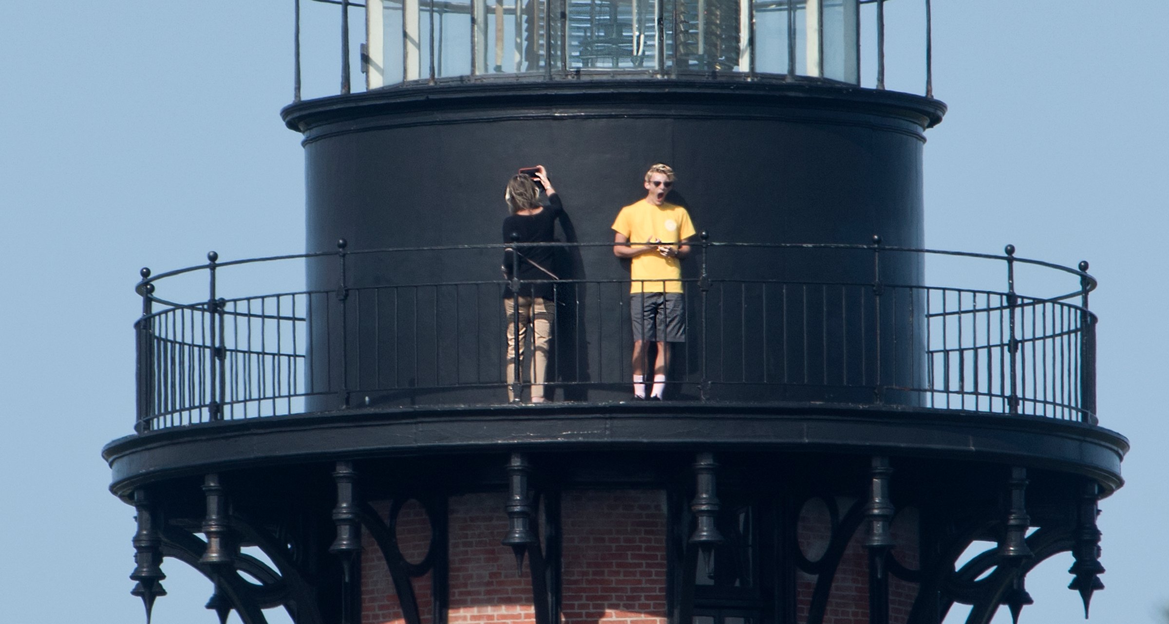 Currituck Beach Lighthouse brick tower rising above the tree line in Corolla, with visitors on the observation platform