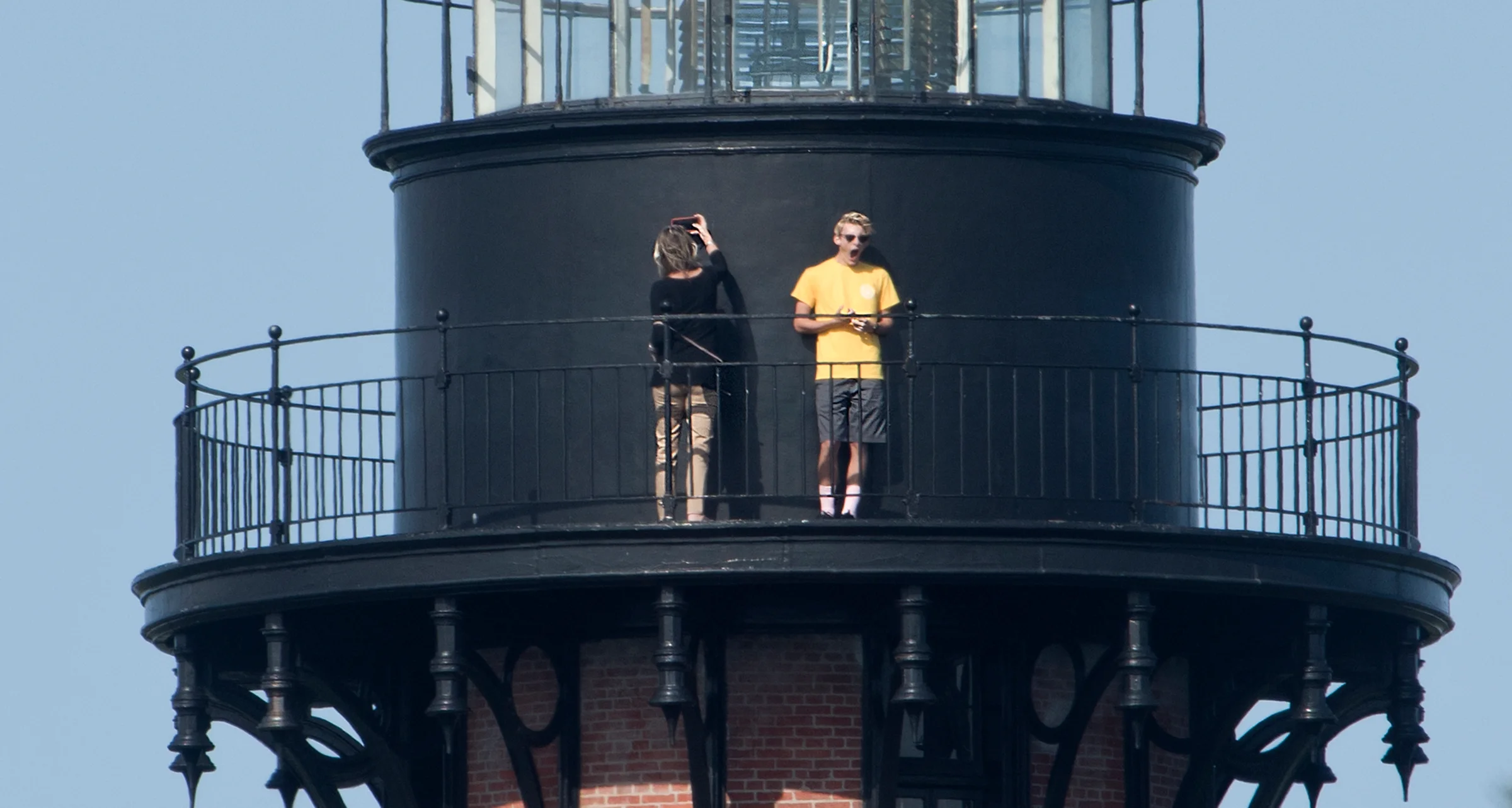 Currituck Beach Lighthouse brick tower rising above the tree line in Corolla, with visitors on the observation platform
